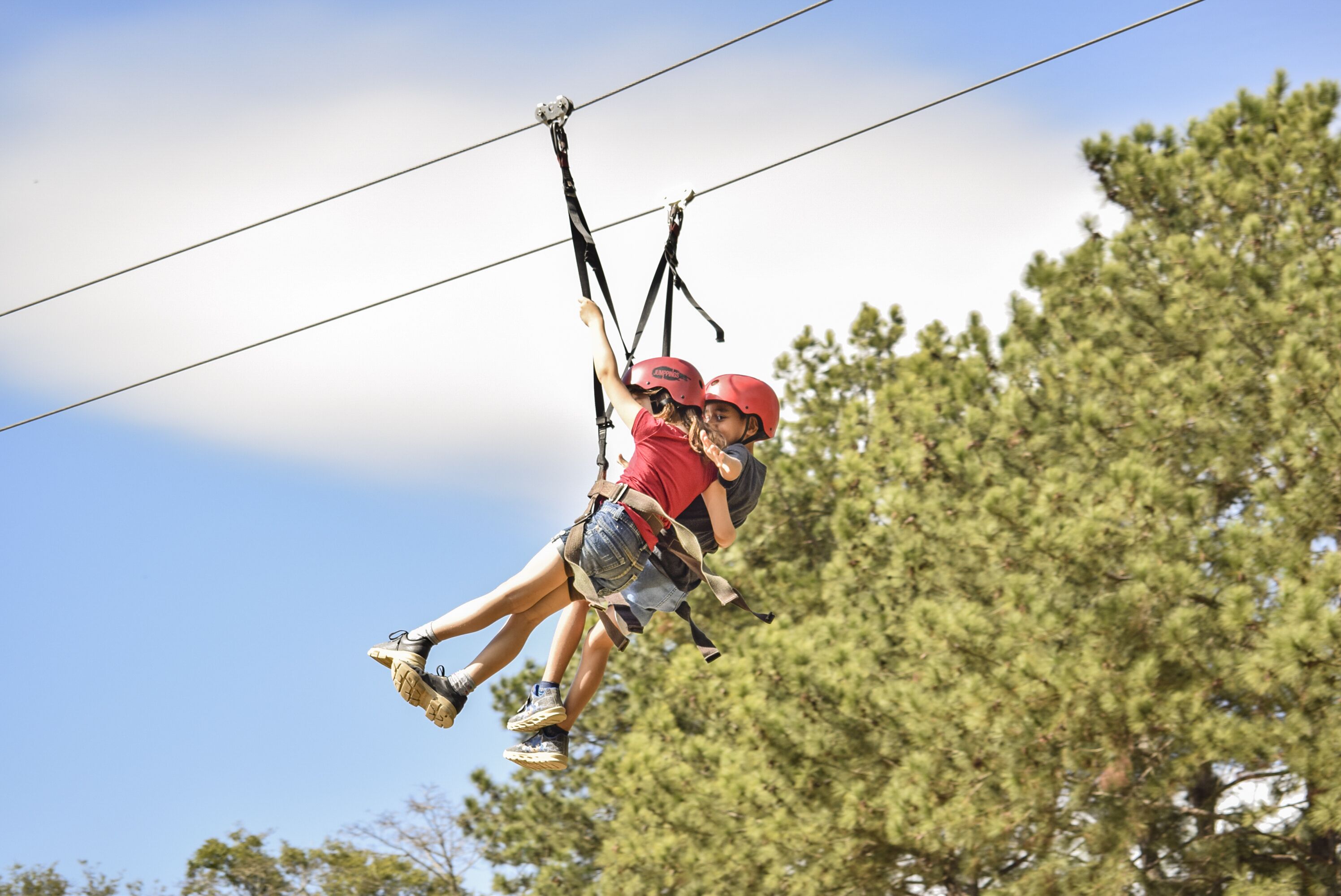 Two people ziplining with safety harnesses, wearing helmets, and surrounded by trees.