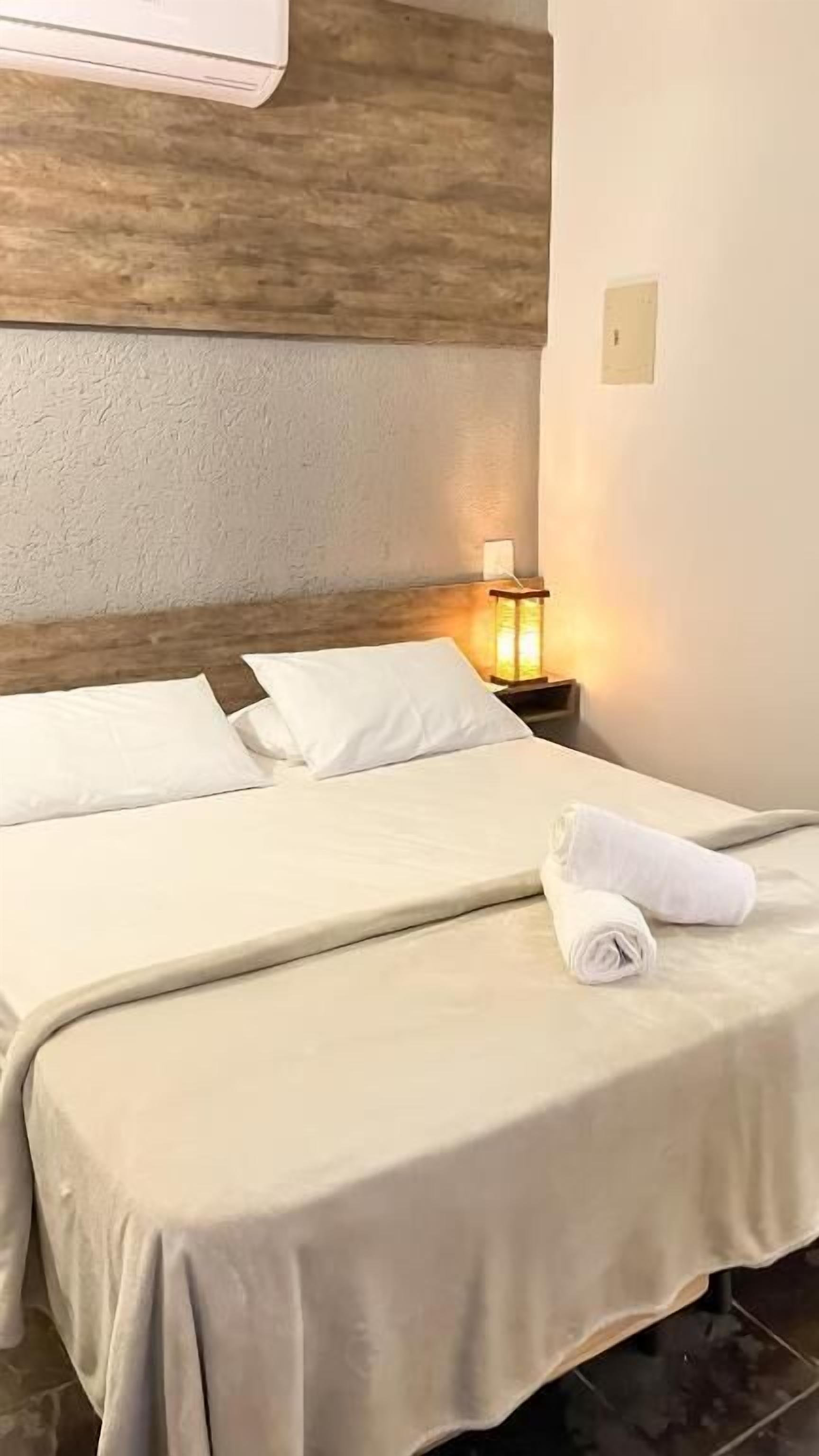 A hotel room with a wooden headboard, a bedside lamp, and neatly made beds with white linens.
