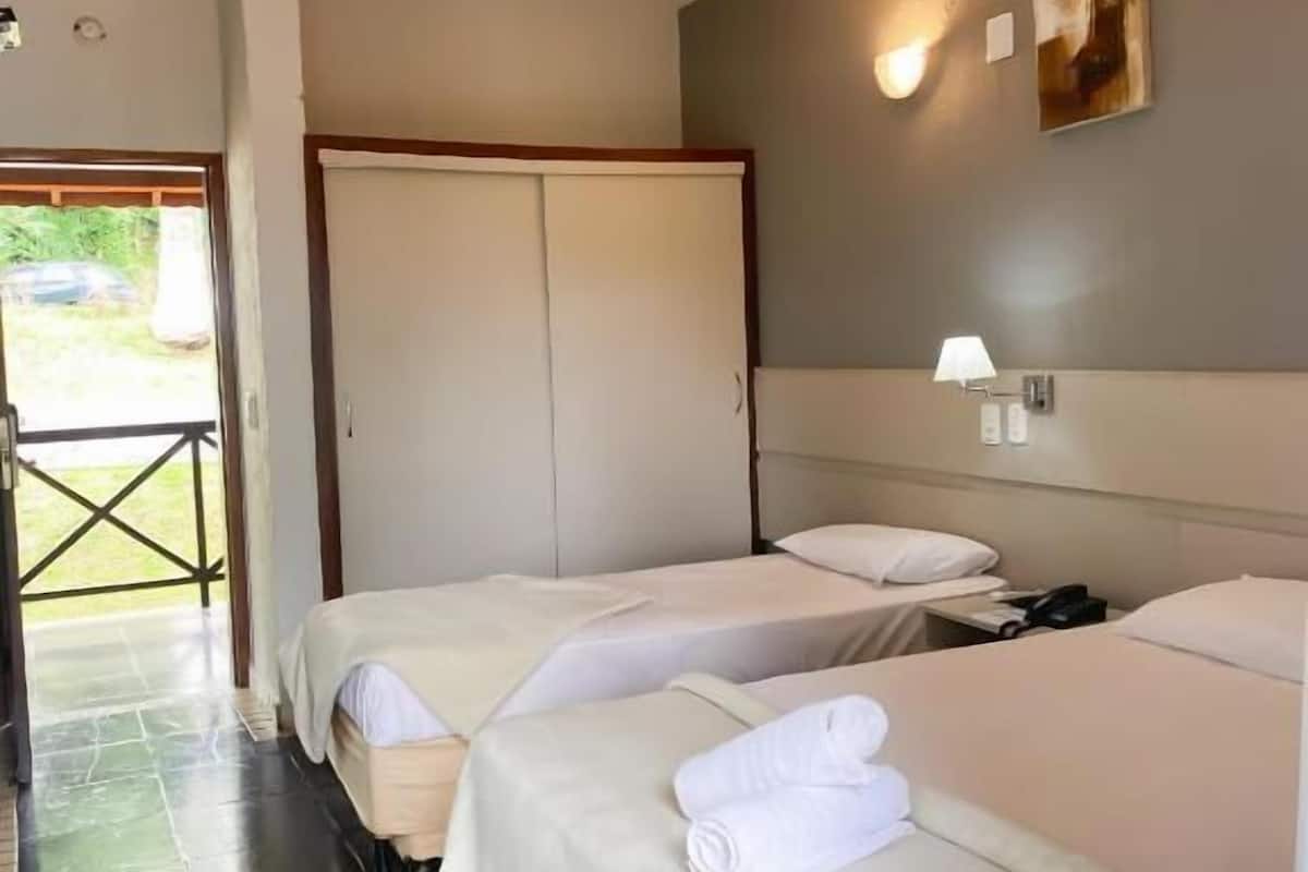 A hotel room with two beds, a wardrobe, a small table, and a wall-mounted lamp.