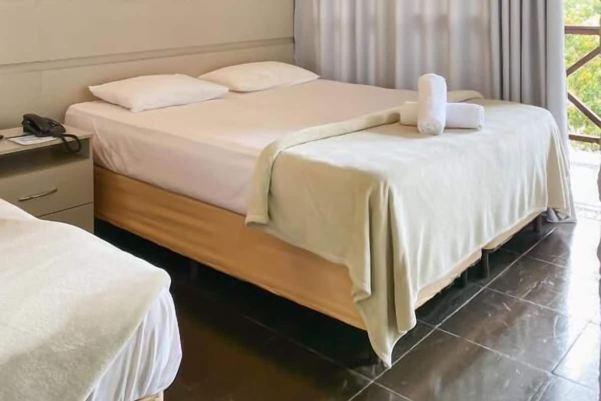 A hotel room with a bed, a bedside table with a phone, and a window with curtains.