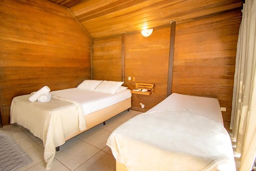 A cozy room with two beds, wooden walls, a small bedside table, and a wall-mounted light fixture.