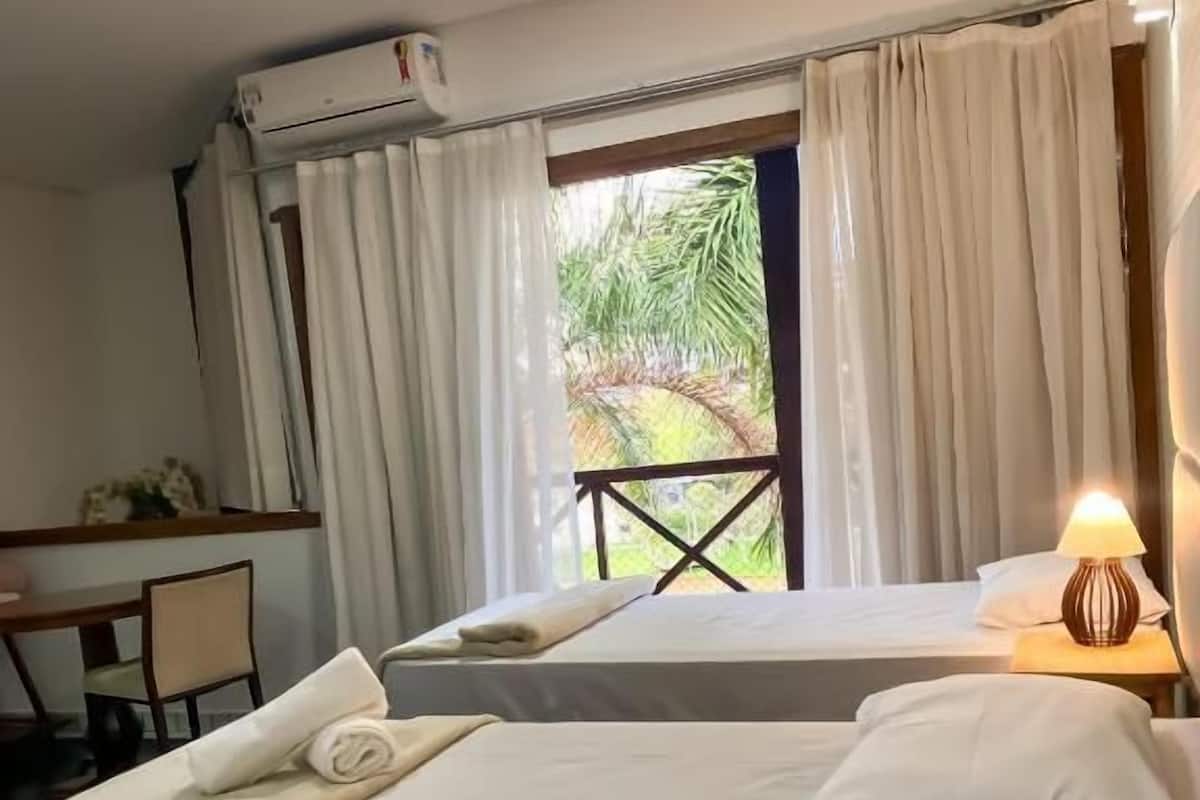 A hotel room with two beds, a desk, and a window with curtains.