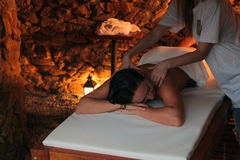 A person receiving a massage in a room with a stone wall and a small table with a towel.