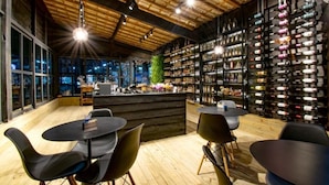 Un bar modern amb sostre de fusta i una paret plena de garrafes de vi. Hi ha taules i caires per seure.