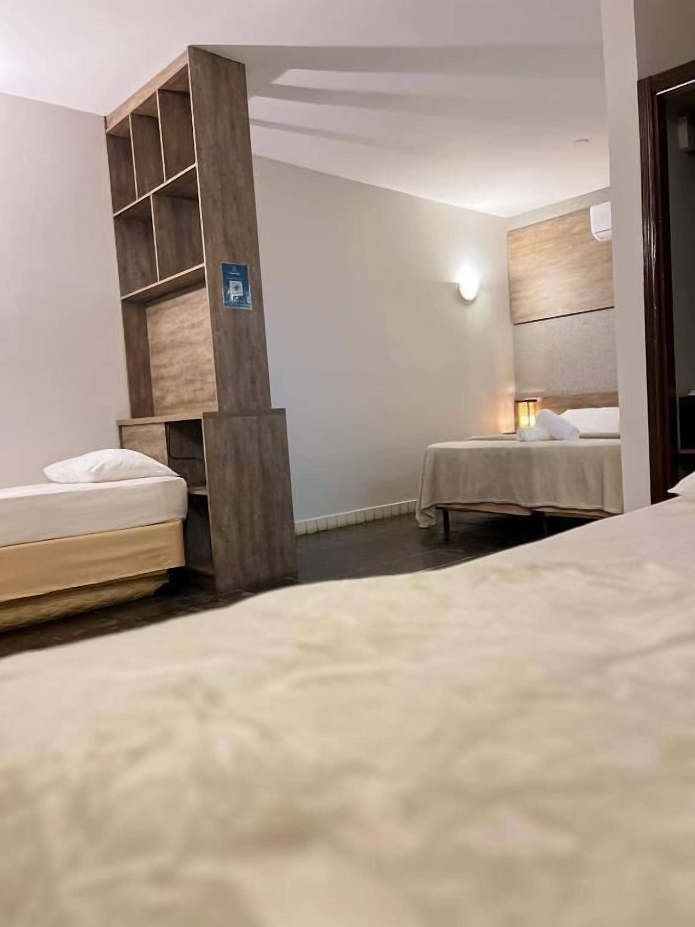 Habitación de hotel con dos camas, un armario de madera, una lámpara de pared y un pequeño cartel en el armario.