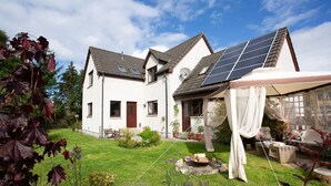 A two-story house with solar panels, a garden, and a patio area.