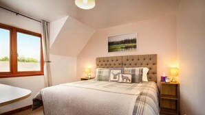 A bedroom with a large bed, a bedside table, a lamp, and a window with curtains.