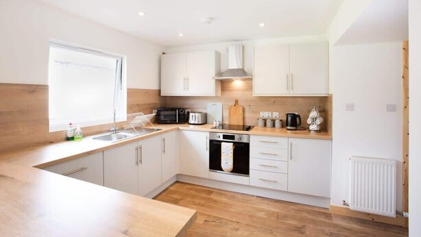 A modern kitchen with white cabinets, a wooden countertop, a built-in oven, and a window providing natural light. - 3BR Cottage w/ Garden, Free Parking for 6 Guests (Ardross)