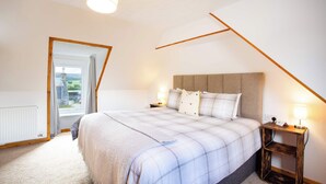 A bedroom with a large bed, a nightstand, a lamp, and a view through a window. - 3BR Cottage w/ Garden, Free Parking for 6 Guests (Ardross)