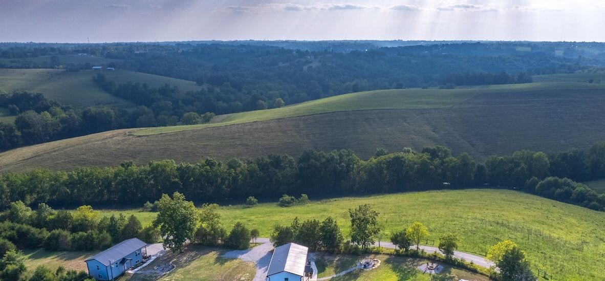 An aerial view of a rural landscape with rolling hills, scattered trees, and a few buildings.