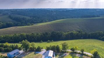 Eine Luftaufnahme einer ländlichen Landschaft mit sanften Hügeln, vereinzelten Bäumen und einigen Gebäuden.