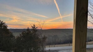 Une vue depuis une terrasse en bois donnant sur un paysage rural, avec des arbres et une route.