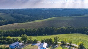 Une vue aérienne d’un paysage rural, avec des collines ondoyantes, quelques bâtiments dispersés et un ciel dégagé.