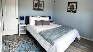 Une chambre à coucher avec un lit, des tables de chevet, un tapis bleu et deux œuvres d’art murales.
