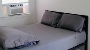 Ein Schlafzimmer mit Bett, einem Fenster mit Jalousien und einem Wandheizkörper.