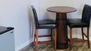 Ein Zimmer mit einer kleinen Küchenzeile, einem runden Holztisch mit vier Stühlen und einem an der Wand montierten Flachbildfernseher.