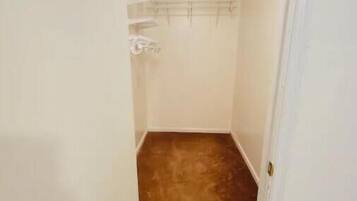 A narrow hallway with a wooden floor leading to a closet with a metal rack.