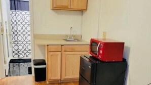 A small kitchen with wooden cabinets, a black refrigerator, and a red microwave. - Private studio next to FT Stewart (Hinesville)