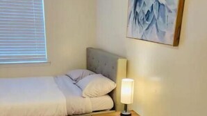 A small, neatly arranged room with a bed, a chair, a table, and a lamp. - Private studio next to FT Stewart (Hinesville)