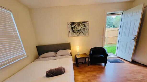 A bedroom with a bed, a nightstand, a chair, and a door leading to an outdoor area. - Private studio next to FT Stewart (Hinesville)