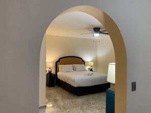 A bedroom with a bed, two bedside tables with lamps, a ceiling fan, and a tiled floor.