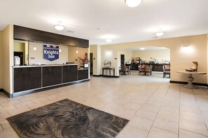 Een receptie met een Knights Inn bord, een receptiebalie, een eetruimte met tafels en stoelen, en een decoratieve muur met een klok.
