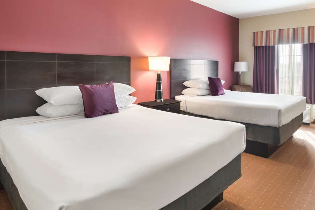 A hotel room with two beds, a nightstand, a lamp, and a window with curtains.