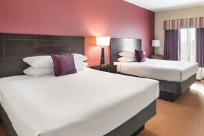 Een hotelkamer met twee bedden, een nachtkastje, een lamp en een raam met gordijnen.