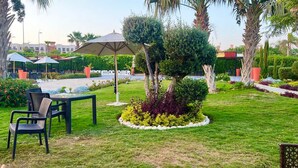 A well-maintained garden area with a seating arrangement including chairs and a table, surrounded by neatly trimmed bushes and a central tree. - Cozy 2 bedroom 1 bathroom. (Giza Governorate)