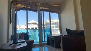 A modern living room with a large sliding glass door leading to a balcony. There is a sofa, a small table, and a TV on a stand. - Cozy 2 bedroom 1 bathroom. (Giza Governorate)