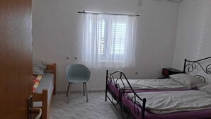 Ein kleiner, sauberer Raum mit zwei Betten, einem Sessel, einem Schreibtisch und einem Fenster mit Vorhängen.