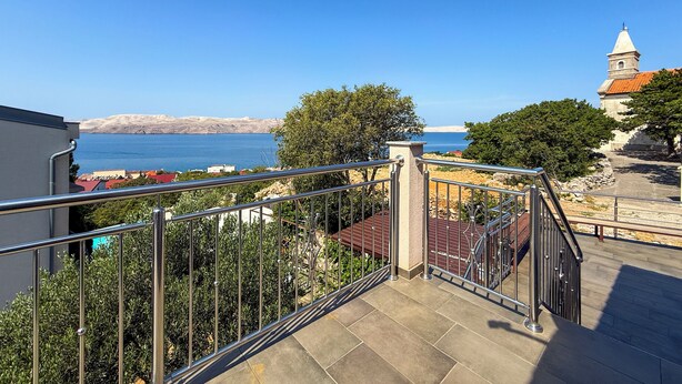 Ein Balkon mit Blick auf das Meer, eine Kirche und eine Steinmauer.