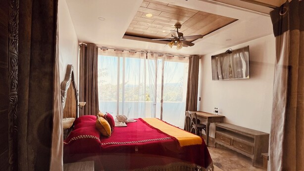 Habitación de hotel con una cama grande, un escritorio, una silla, un televisor y vistas al exterior.