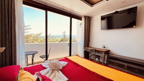 Habitación de hotel con cama, escritorio, televisión y balcón con vistas.