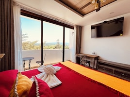 Habitación de hotel con cama, escritorio, televisión y balcón con vistas.