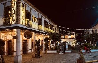 A historic building with a sign reading "HOTEL" and "El Rey." It features a balcony with string lights and a statue of a cowboy.