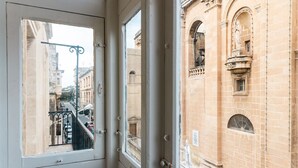 Blick durch ein Fenster auf ein Gebäude mit klassischer Architektur, darunter Rundbogenfenster und eine Statue.