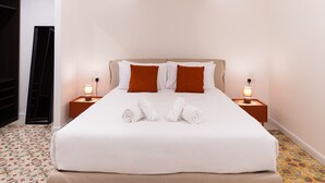 Ein ordentlich bezogenes Bett mit weißen und braunen Kissen, zwei Nachttischlampen und aufgerollten Handtüchern.