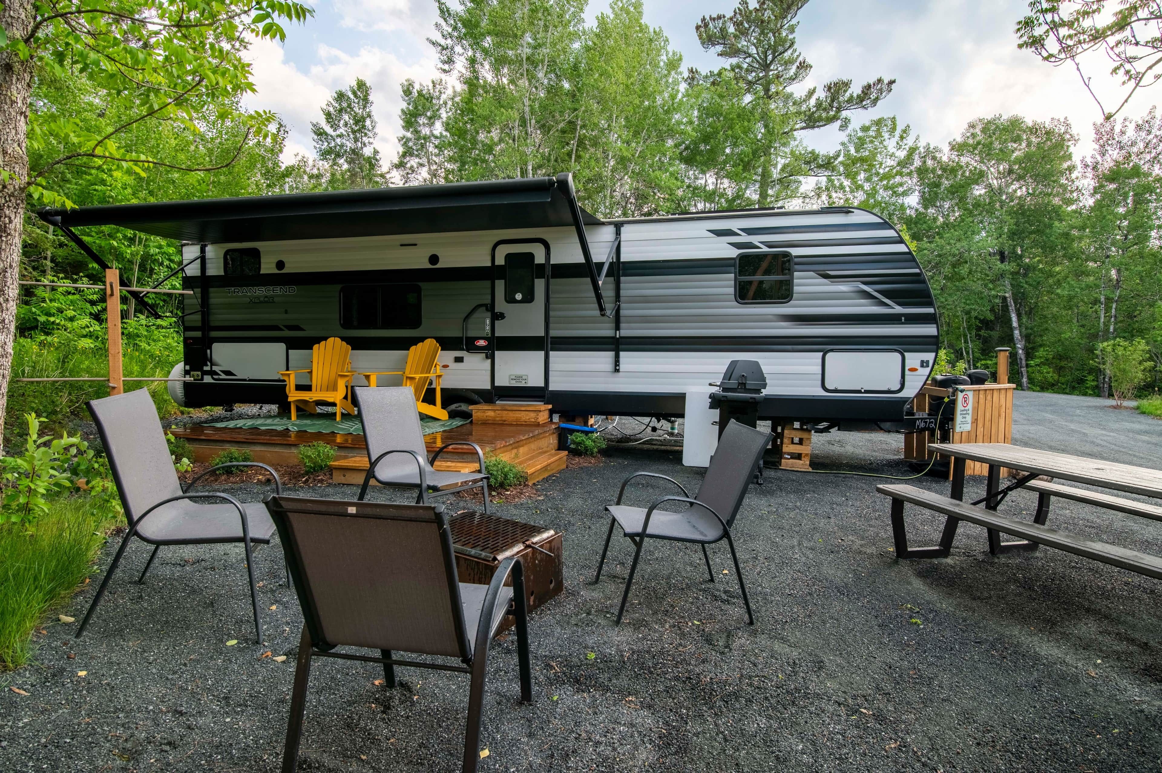 A recreational vehicle (RV) with a covered porch area, outdoor seating, and a picnic table.