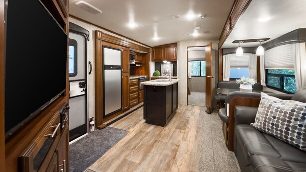 Une cuisine bien éclairée dans un camping-car, avec des meubles en bois, un réfrigérateur en acier inoxydable et un îlot central doté d’un évier.