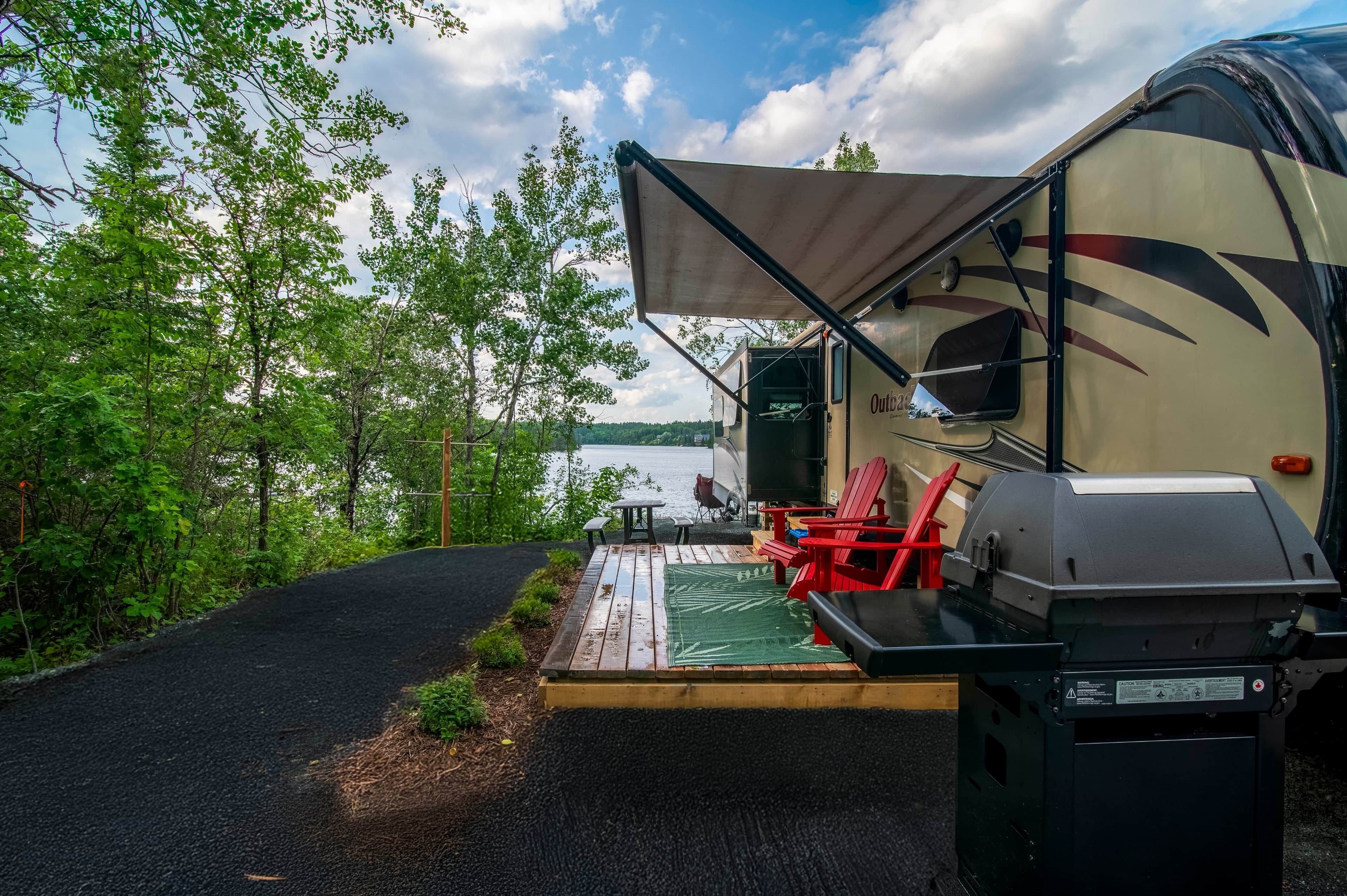 A campsite with a covered outdoor seating area, a grill, and a view of a lake.