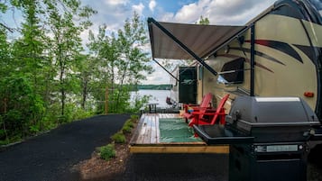 A campsite with a covered outdoor seating area, a grill, and a view of a lake.