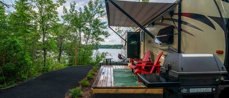 A campsite with a covered outdoor seating area, a grill, and a view of a lake.