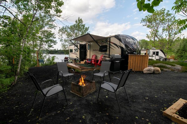 A campsite with a covered RV, outdoor seating, and a fire pit. - RV 7 Corner Unit W/ Full Privacy and Panoramic Views (Kenora)