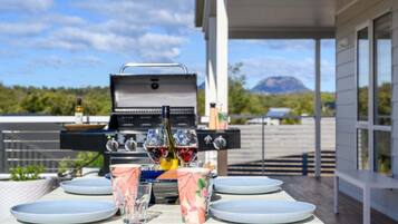 An outdoor dining area with a grill, wine glasses, and plates set on a table.