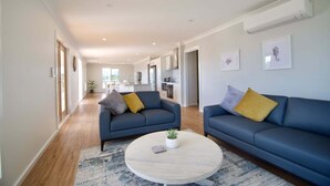 A spacious living area with two sofas, a round coffee table, and a kitchen in the background. - Ambience - Freycinet Holiday Houses (Coles Bay)