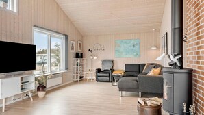 A modern living room with a large TV, wooden flooring, a fireplace, and a view through large windows. - Lovely home in Thisted with kitchen (Thisted)