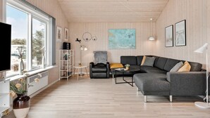 A modern living room with a large window, a grey sectional sofa, a black leather chair, and a white floor lamp. - Lovely home in Thisted with kitchen (Thisted)