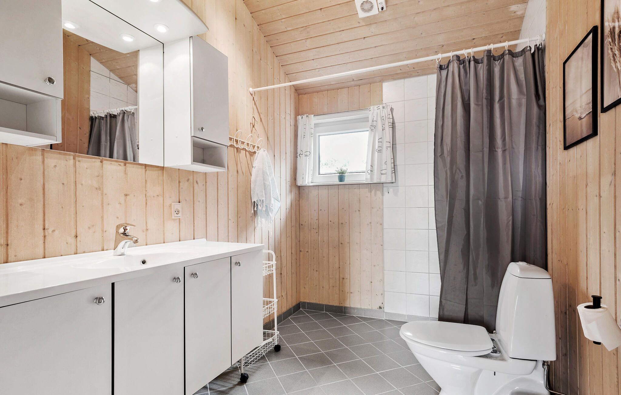 Un baño moderno con paneles de madera, un lavamanos blanco, inodoro y cortina de ducha.