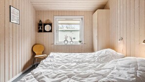 A bedroom with a wooden slatted ceiling, a single bed, a wooden chair, a window with a view of a building, and a shelf with decorative items. - Lovely home in Thisted with kitchen (Thisted)
